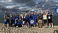 Gruppenfoto der DPolG Berlin nach dem „Lauf zwischen den Meeren 2026“ am Ostseestrand in Damp. Die Läuferinnen und Läufer stehen mit ihren Finisher-Medaillen im Sand, halten DPolG-Fahnen in die Höhe und jubeln gemeinsam. Zwei Teilnehmende machen einen Handstand, während die Gruppe fröhlich für das Erinnerungsfoto posiert. Im Hintergrund sind die Ostsee, ein bewölkter Himmel und die Küstenlandschaft zu sehen. Das Bild vermittelt Teamgeist, Freude und den erfolgreichen Abschluss der 92,2 Kilometer langen Staffel von Husum nach Damp.