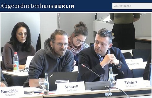 Anhörung im Abgeordnetenhaus Berlin: Frank Teichert (DPolG Berlin) sitzt am Tisch im Ausschusssaal und verfolgt die Diskussion zum Berliner Datenschutzgesetz neben weiteren Sachverständigen und Teilnehmenden, hier links Arne Semsrott von FragdenStaat